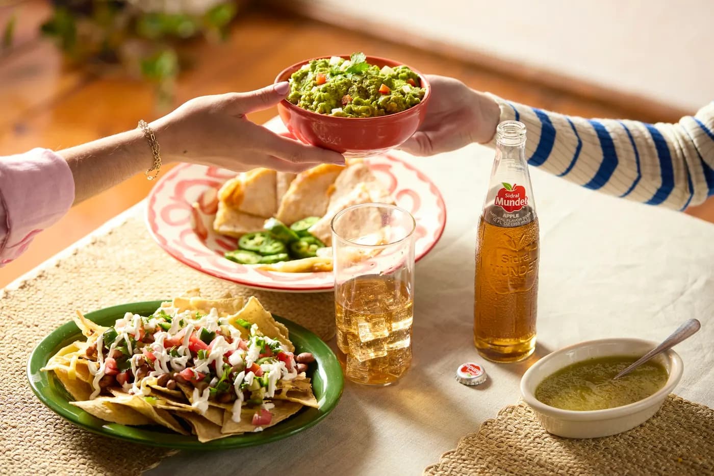 Hands passing plates of tacos across a table